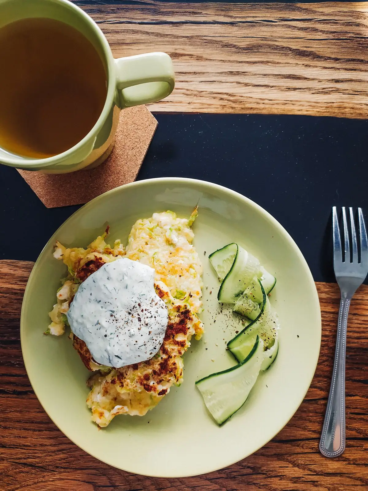 Golden egg fritters on a plate with sliced cucumber and a cup of tea