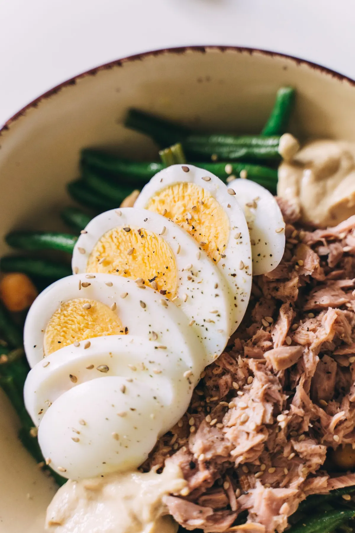 Halved boiled eggs on tuna and green beans in a bowl
